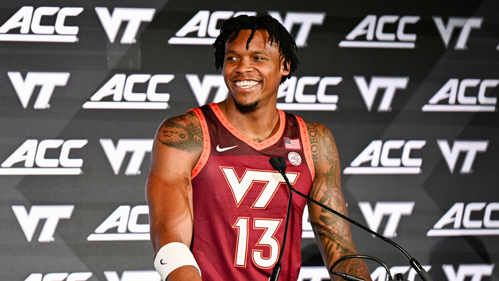A basketball player in a maroon Virginia Tech jersey stands at a podium with an ACC logo, smiling during a press event.